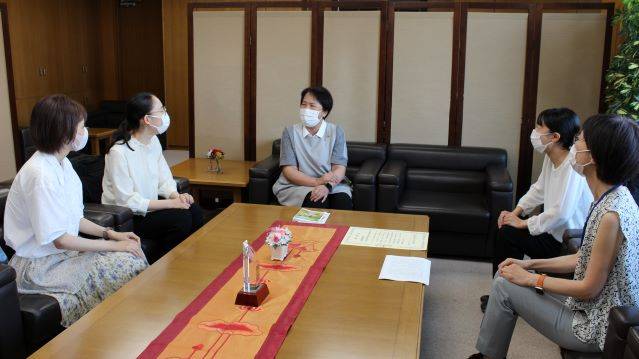 岡本学長と豊沢准教授と学生が机を囲んで椅子に座っている